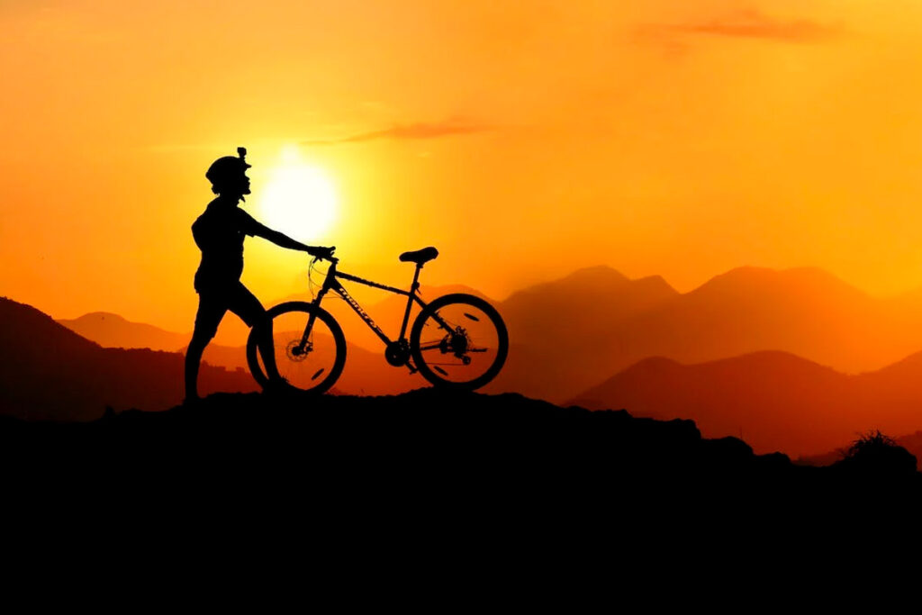 mountain bike - homem em pé no alto da montanha segurando sua mountain bike contemplando o por do sol